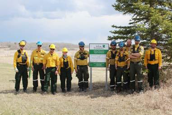 Portrait of ten people in protective gear standing in a parkland landscape.
