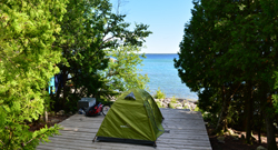 A green tent is on a wood platform on the shoreline
