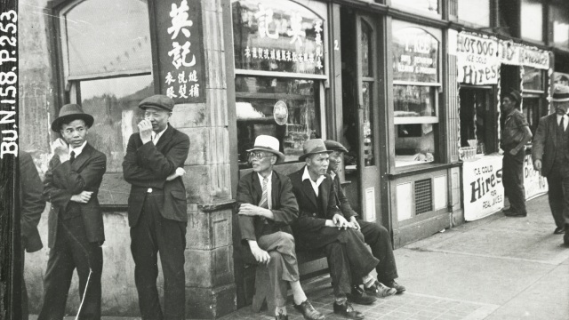 Black and white photo of a few men standing near the corner of a building