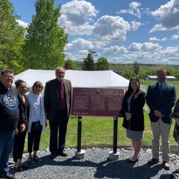 A group of people beside a commemorative bronze plaque in an outdoor setting