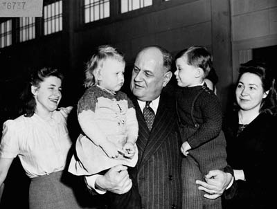 Historical photo of two kids in the arms of a man smiling