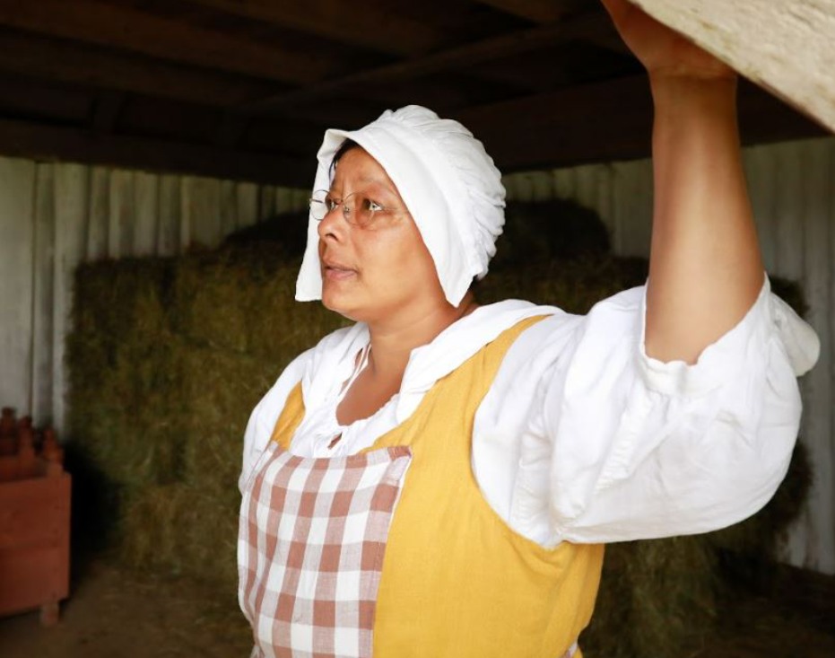 A woman in historical clothes inside a barn