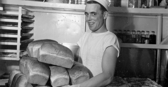 Photo of baker in galley of HMCS Haida with many loaves of bread