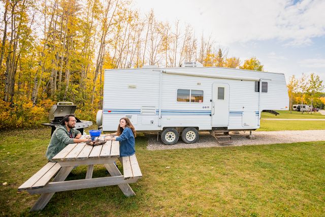 Two visitors sit at a picnic table in front of their RV at an RV park