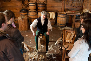 A cooper in period costume is demonstrating the traditional barrel-making process.