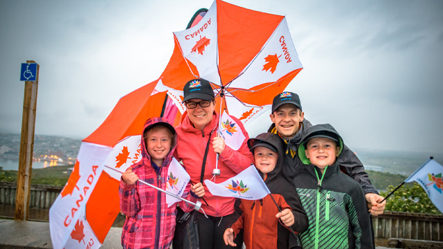 a family of five holding Canadian flags and Canada umbrellas