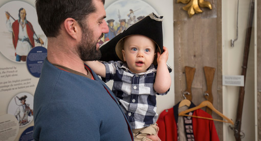  A man holds a baby who is wearing a tricorne hat.