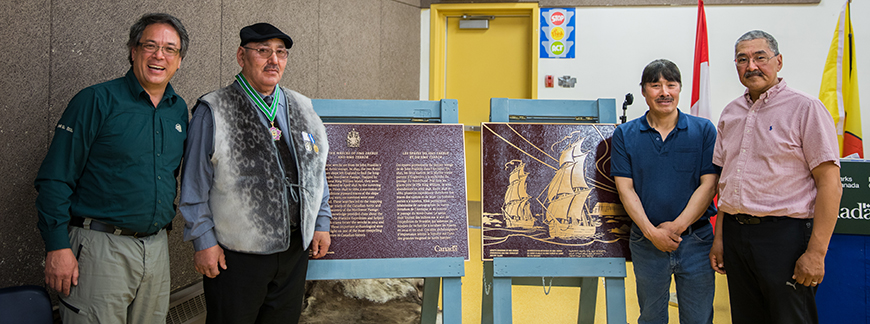 Four men standing together with two burgundy plaques commemorating the national historic site