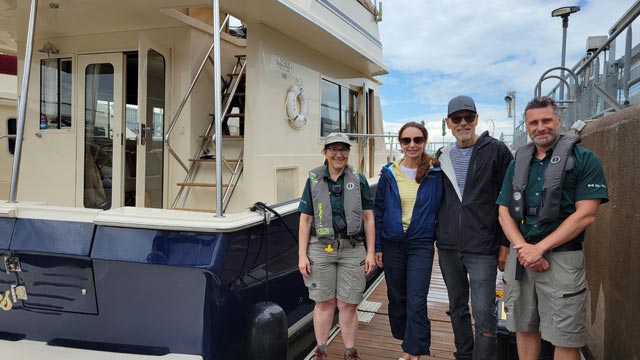 Two Parks Canada lock employees accompanied by a smiling man and woman stand by their boat.