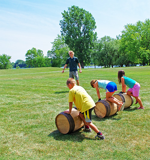 Tree kids rolling wood barrels on the grass