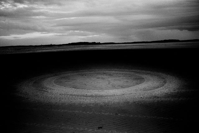 Black and white photo of circular tires marks on the ground.