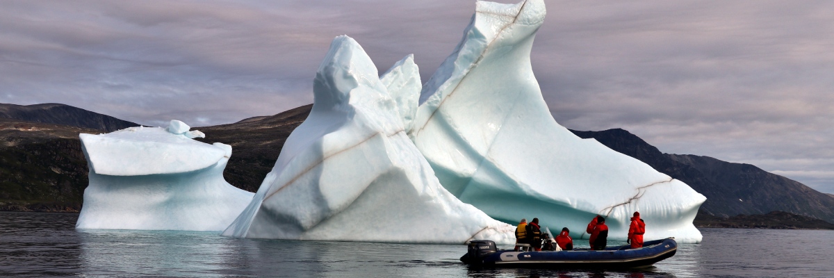 An inflatable boat with 5 crew on board cruise past a large iceberg.