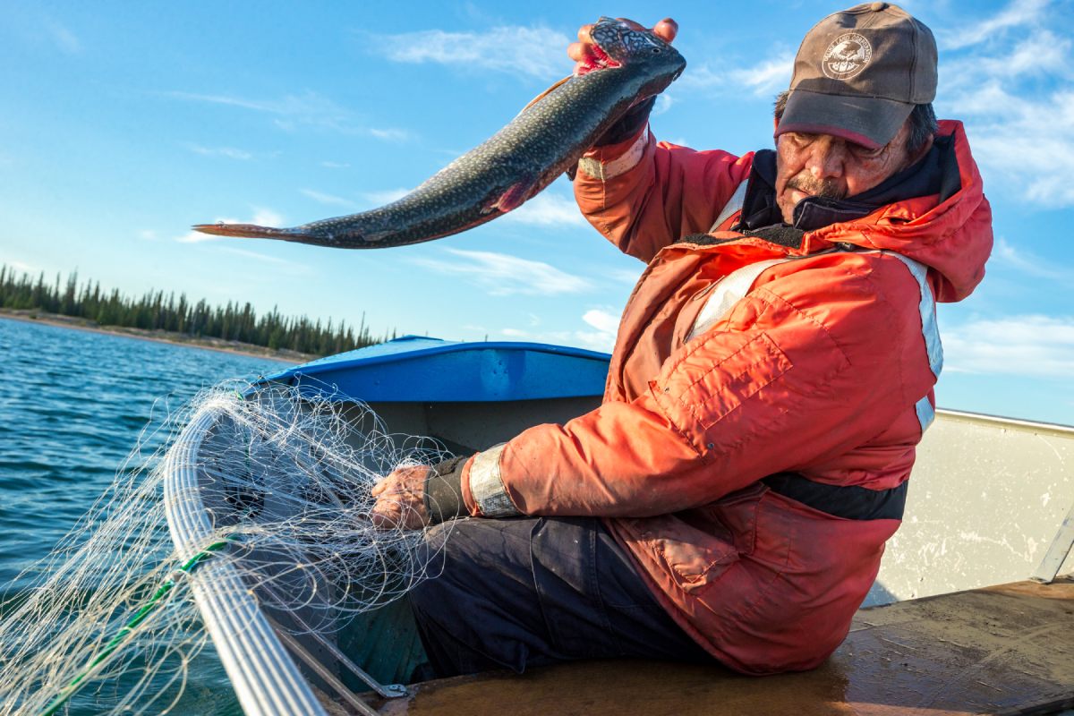 A man hauls a large fish from his net that he’s pulled over the side of his small boat on the water.