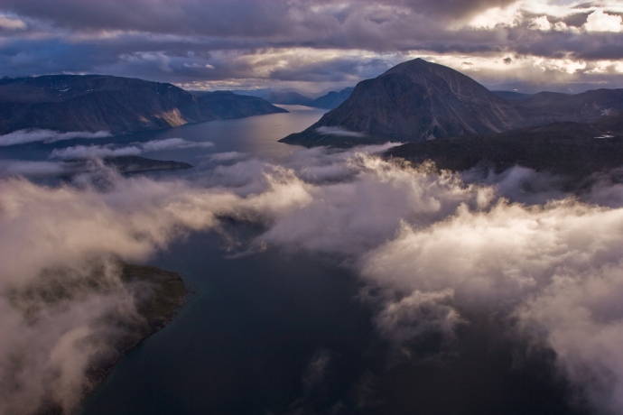 An aerial view from above low lying clouds of a fjord and mountainous landscape.