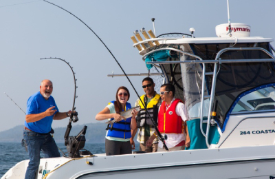 Four people aboard a charter fishing boat smile at the camera. One holds a rod while another holds a fish.