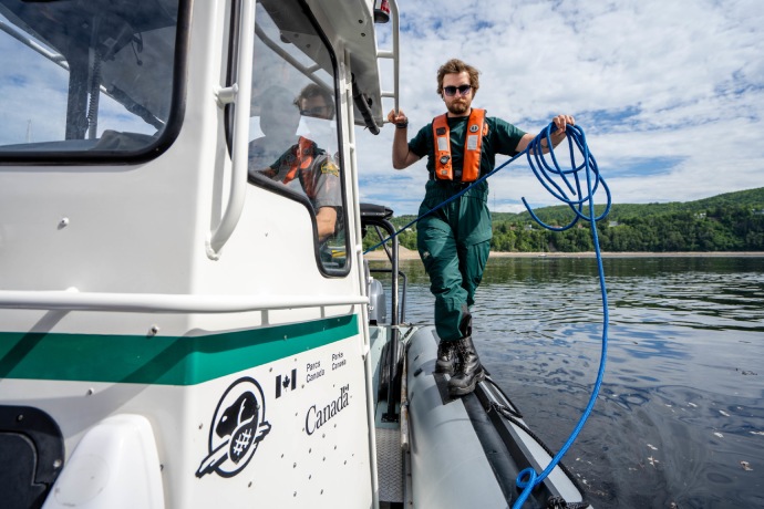 A Parks Canada staff person walks along the edge of a vessel on the water while holding a rope.