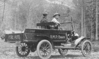 Old fire truck with two men on a dirt road with trees and mountains in the background