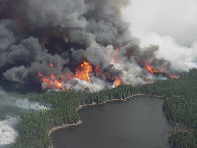 Crown fire with grey and white smoke rages near a lake