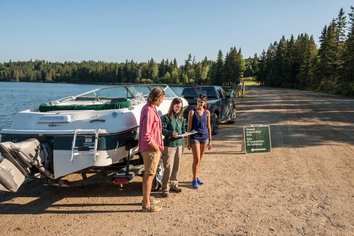 One Parks Canada staff member goes over a checklist with two visitors and their boat at a lakeside inspection station.
