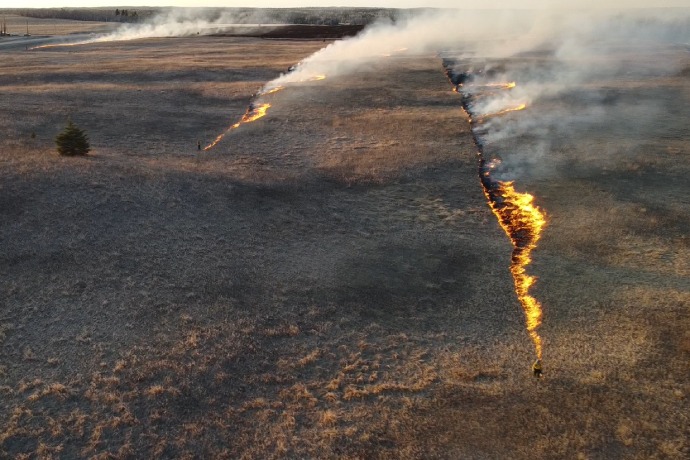 An aerial view of a prescribed fire burning across a grassy plain.