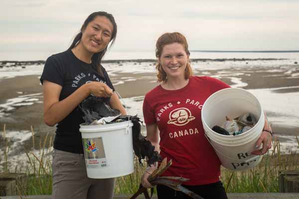 Two people holding buckets, cleaning up a beach.