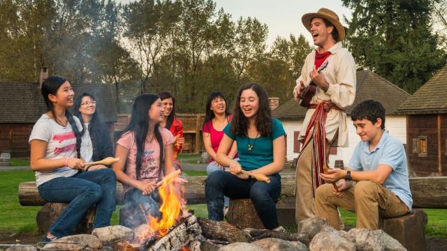 A group of visitors with a costumed guide in front of a fire.