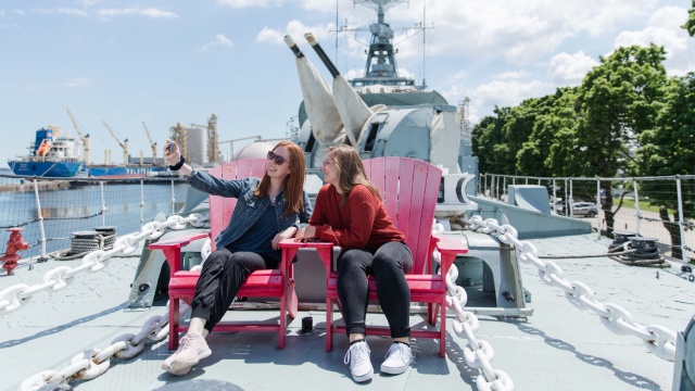 Two young women on Parks Canada’s red chairs on the deck of the destroyer HMCS Haida.
