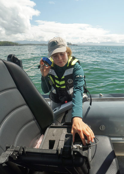 A Parks Canada staff member onboard a boat on the water listens to a device that helps her hear underwater noises.