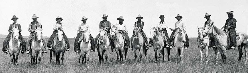 Eleven cowboys lined up, sitting on their horses.