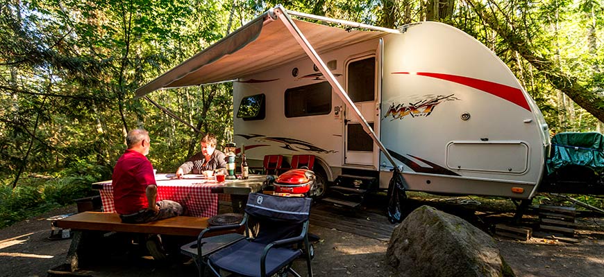 A couple relax outside their RV, surrounded by the lush forest at Prior Centennial campground on Pender Island