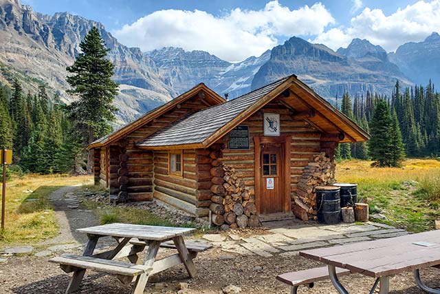 The Elizabeth Parker hut sits in an open meadow with mountains towering behind it.
