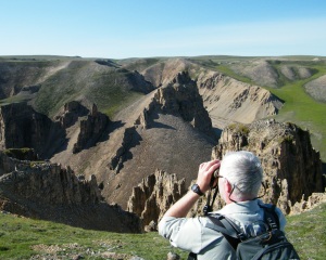 man looking at cliffs through binoculars