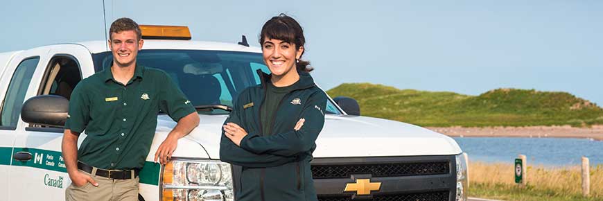 Two PEI National Park staff members are smiling and standing in front of a Parks Canada truck in Covehead. 