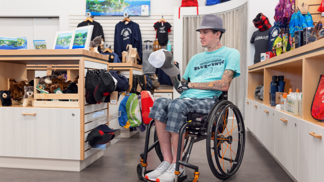 A man in a wheelchair holds a cap in a shop.