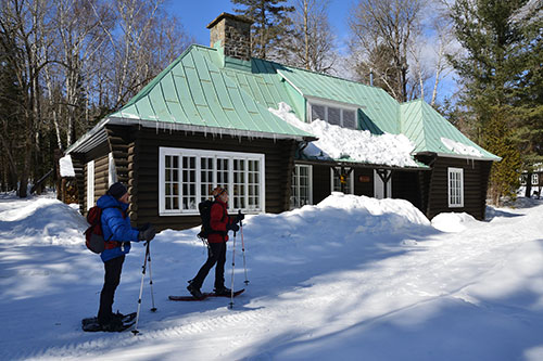 Two snowshoers in front of the Wabenaki-Andrew cottage