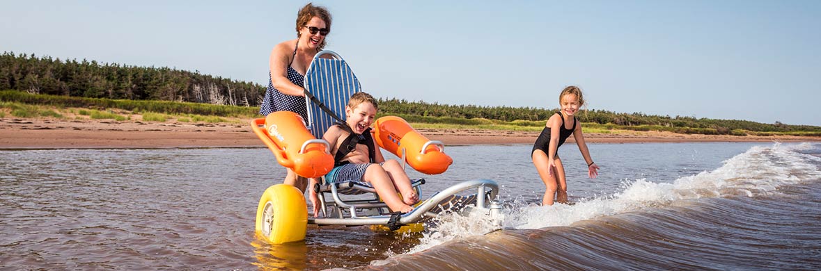 A family plays in the wakes, including a young boy in a beach wheelchair