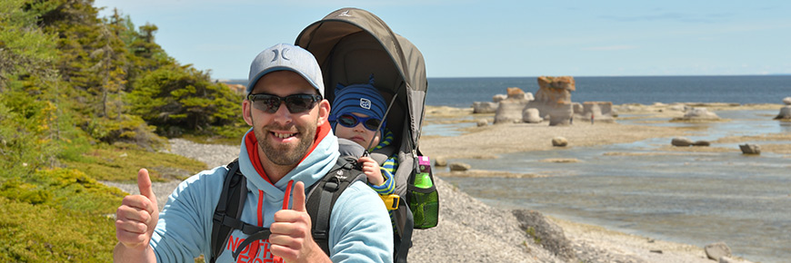 Photograph of a father with his child in a baby backpack with monoliths and the sea in the background