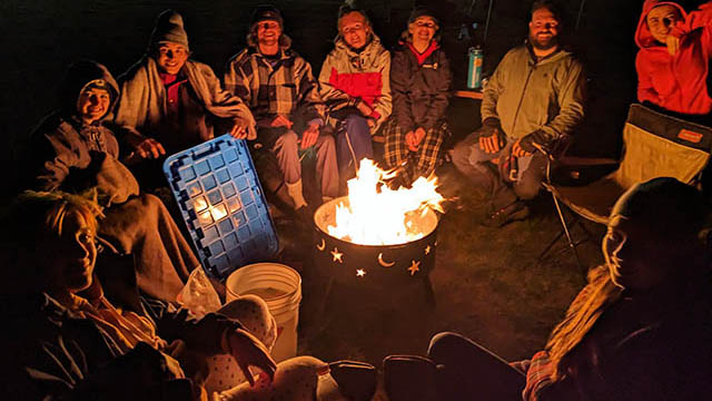 A group sits around a campfire at night.