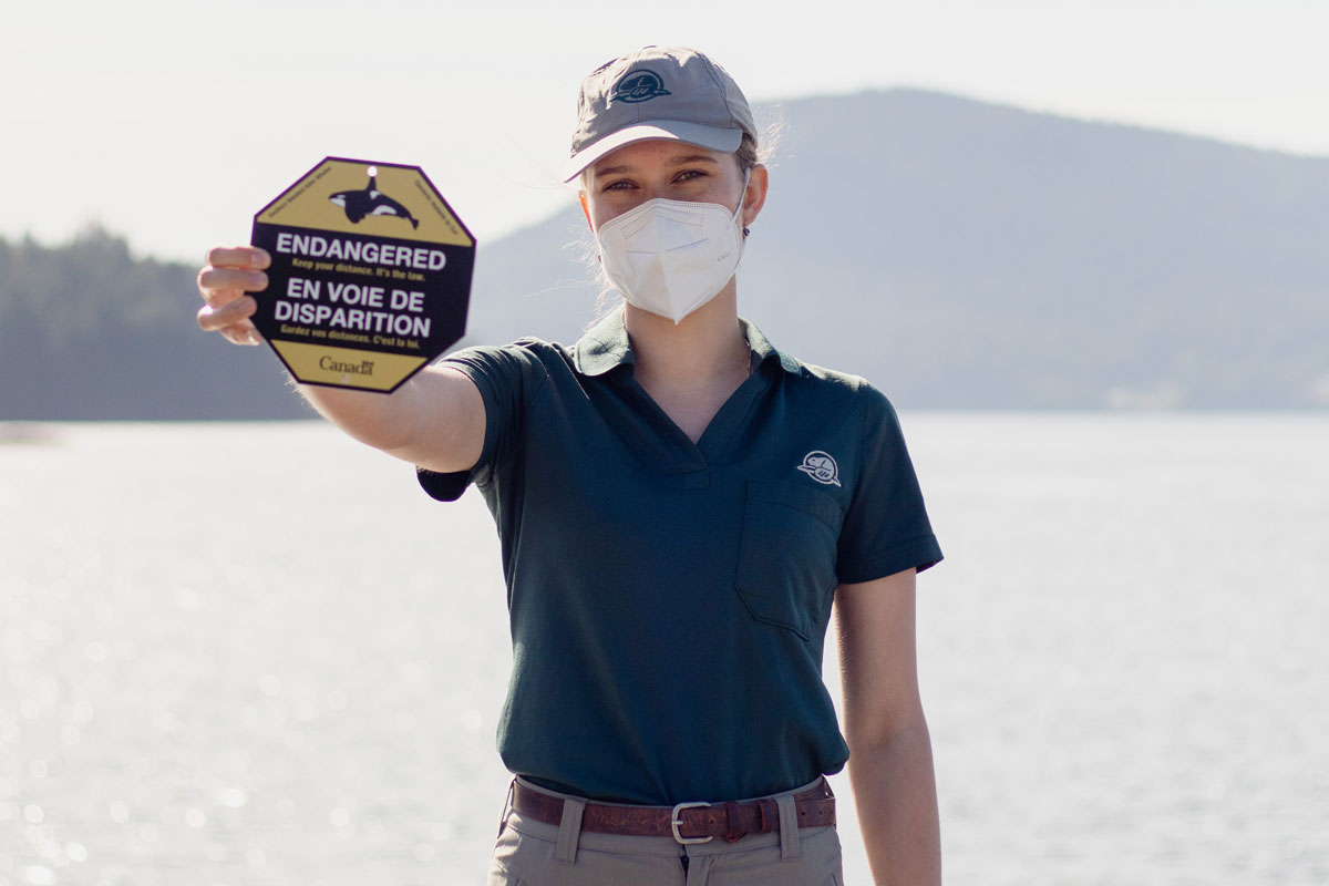 Parks Canada team member holding a sign that says “Endangered: keep your distance. It’s the law”