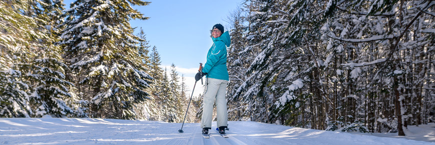 A woman cross-country skis on a trail through coniferous forest.