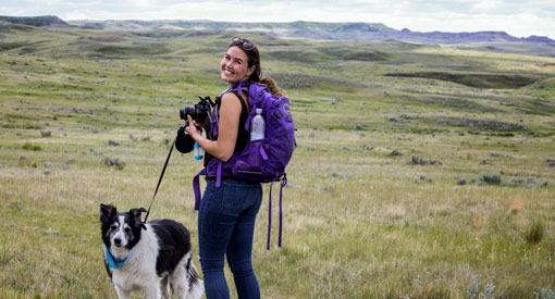 Woman takes pictures of the Grasslands while on a hike with her dog.