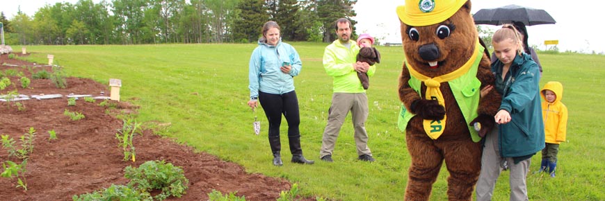 A Parks Canada staff member and Parka mascot show a garden to a family in Fundy National Park.