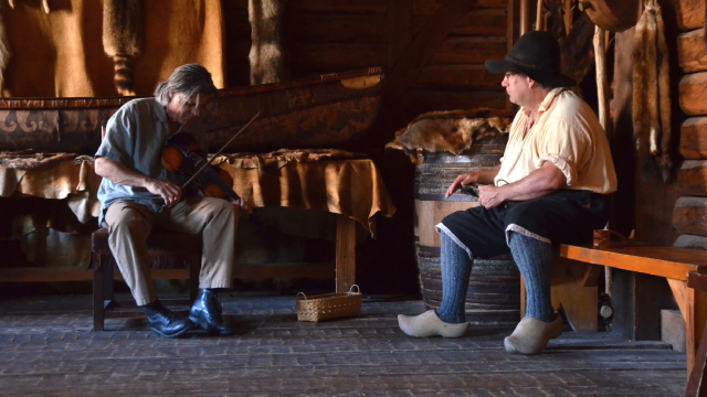 Two musicians put on a musical show in a historic building, one playing a fiddle, the other playing a percussion instrument. 