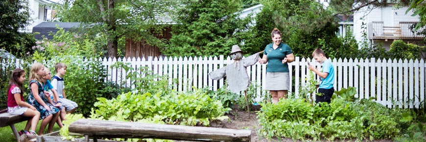 A child helps a Parks Canada staff member pull carrots from the garden as other children watch.