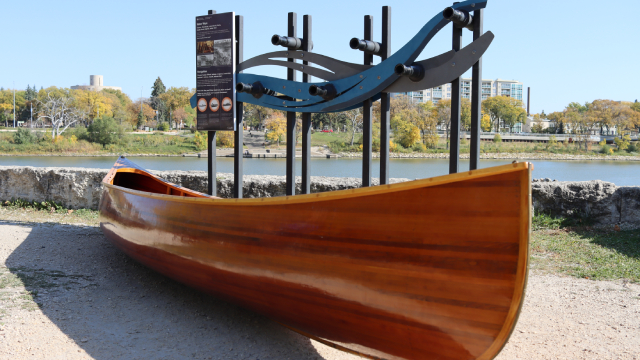 A canoe and interpretive panels, installed outdoors on dry land.