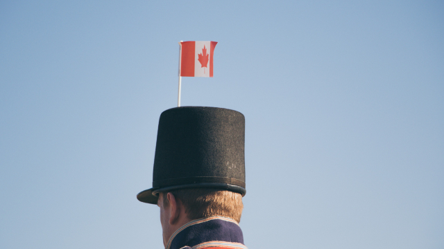 The back of a soldier in costume's head, with a mini canada flag on the top of his hat. 