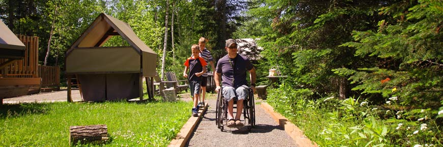 A father with two kids on the barrier-free path next to an oTENTik tent with a wheelchair-friendly ramp access.