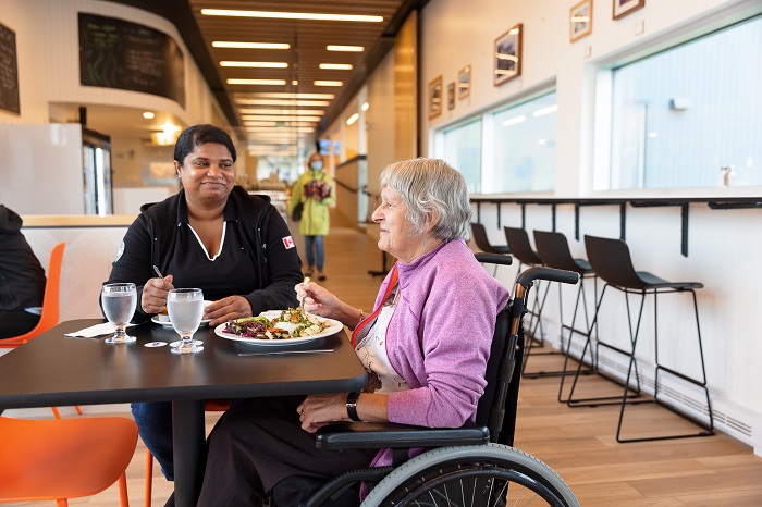 Two women, one in a wheelchair, share a meal at the food service.