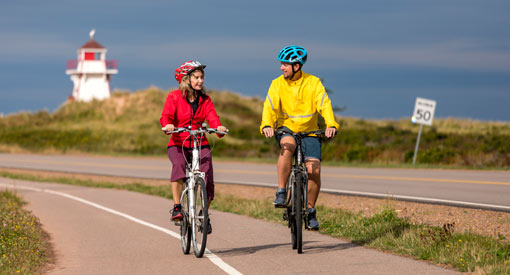 Two cyclists ride along the Gulf Shore Way, Covehead lighthouse in the background.