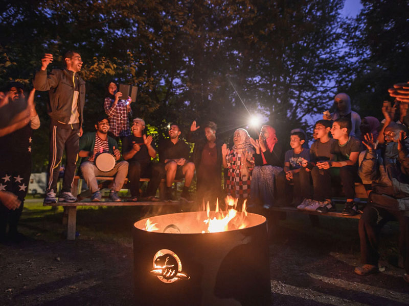 New Canadians enjoying themselves, making music and dancing around a group fire pit. 